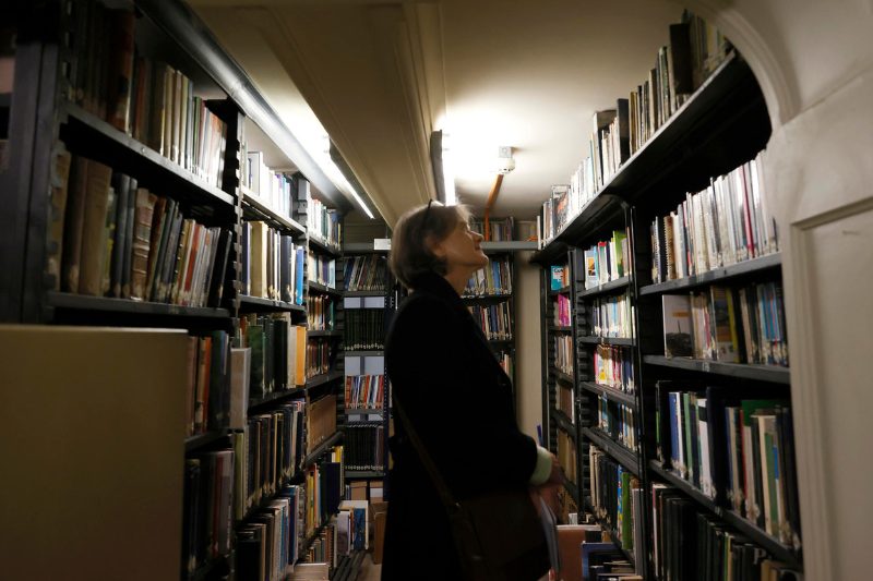 Mujer de pie mirando las estanterías con libros en una sala de biblioteca
