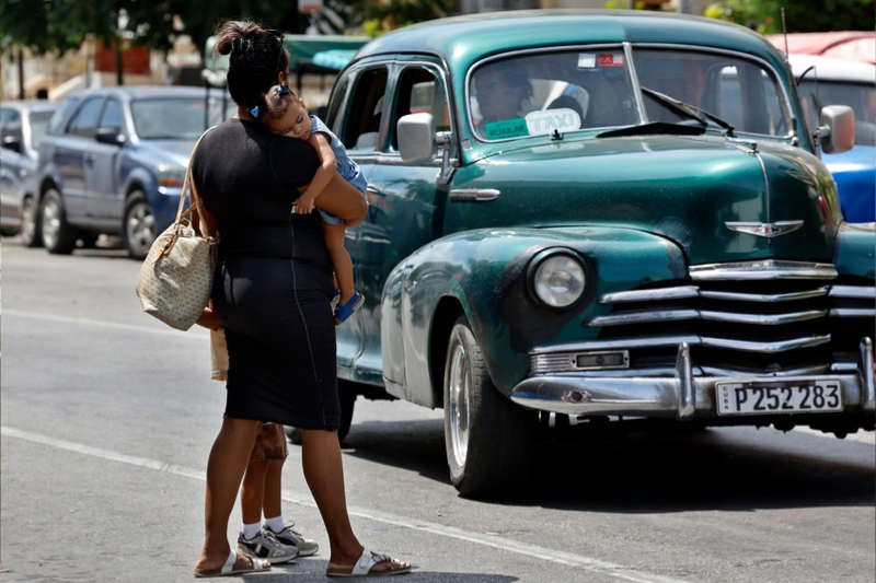 Una mujer cruzando una calle con una niña en sus brazos en La Habana (Cuba)